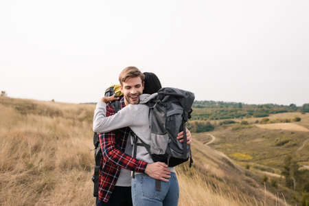 Smiling traveler with backpack embracing african american woman during tripの写真素材