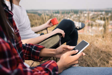 Cropped view of african american woman holding smartphone while sitting near boyfriend with cup on lawnの写真素材