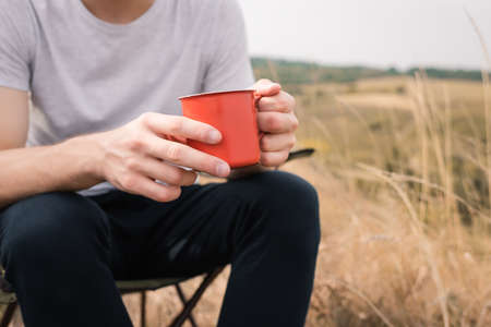 Cropped view of man holding cup while sitting on chair on lawn