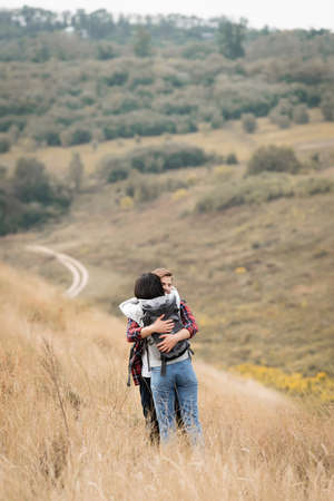 Young man hugging girlfriend with backpack during trip on hillの写真素材