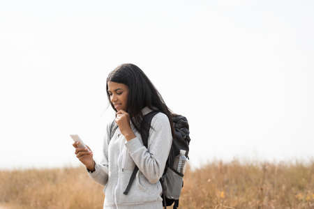 Pensive african american woman with backpack using smartphone outdoors