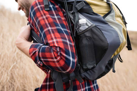 Cropped view of smiling tourist with bottle of water in backpack walking outdoorsの写真素材