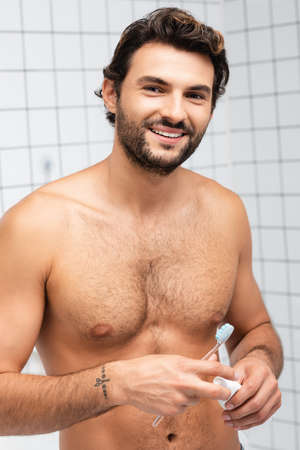 Muscular man smiling at camera while holding toothbrush and tube of toothpasteの写真素材