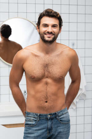 Muscular man in jeans smiling at camera in bathroomの写真素材