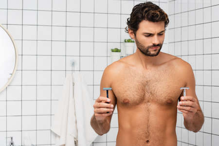Muscular man holding razors in bathroom at homeの写真素材