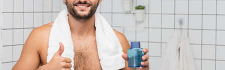 Cropped view of smiling man with towel showing like while holding bottle of after shaving lotion, bannerの写真素材