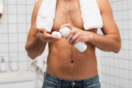 Cropped view of shirtless man with towel squeezing shaving foam in bathroomの写真素材