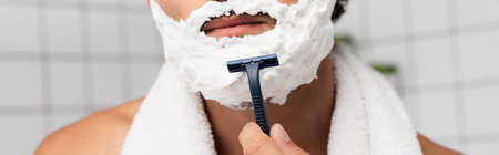Cropped view of man with shaving foam on face holding disposable razor, bannerの写真素材