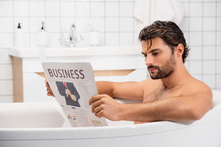 Bearded man reading business newspaper while taking bathの写真素材
