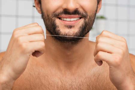 Cropped view of bearded man smiling while holding dental floss in bathroom