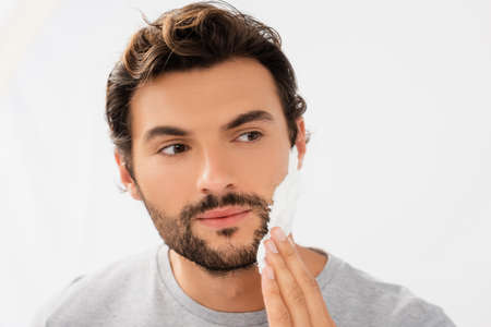 Young bearded man applying shaving foam isolated on grayの写真素材