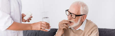 geriatric nurse holding pills and water near aged man, bannerの写真素材