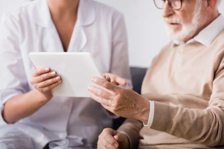 cropped of social worker showing digital tablet to aged man at homeの写真素材