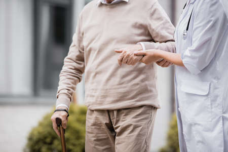 cropped view of social worker supporting aged man strolling with walking stickの写真素材