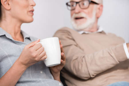 woman holding cup of tea while talking to surprised father on blurred backgroundの写真素材
