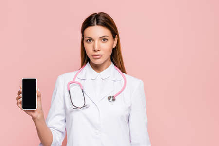 Doctor with stethoscope showing smartphone with blank screen isolated on pinkの写真素材