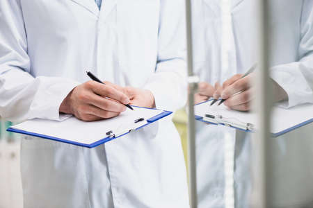 cropped view of pharmacist holding pen while writing on clipboardの写真素材
