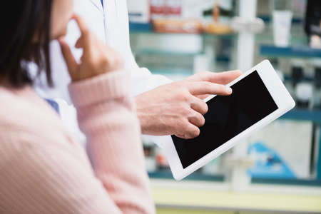 cropped view of pharmacist pointing with finger at digital tablet with blank screen near customerの写真素材