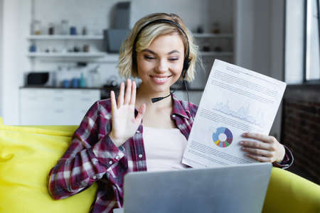 young blonde woman in headphones showing graphs and waving hand