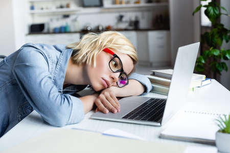 tired blonde woman in eyeglasses working from home and lying on tableの写真素材