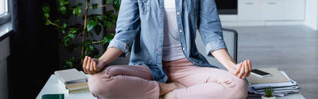 cropped view of woman sitting in lotus pose on table, horizontal banner
