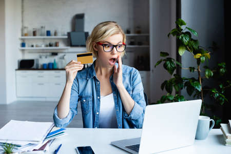 shocked blonde woman in eyeglasses making purchase online