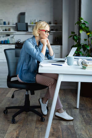 full length of young blonde woman in eyeglasses working from homeの写真素材