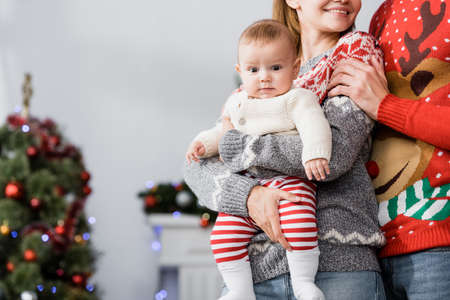 happy woman holding in arms baby boy near husband and blurred christmas tree on backgroundの写真素材