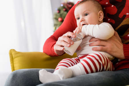 father feeding infant son while holding baby bottle with breast milk