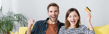 happy woman holding credit card near excited husband, banner