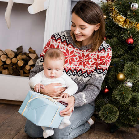cheerful woman holding present near baby boy and decorated christmas tree