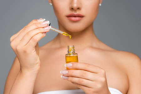 cropped view of woman holding bottle with serum isolated on gray