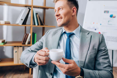 Young businessman smiling while holding cup of coffee in office