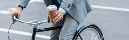 Cropped view of businessman holding coffee to go while cycling outdoors, bannerの写真素材