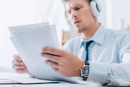 Documents in hands on businessman listening music in headphones on blurred backgroundの写真素材