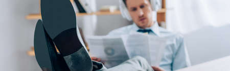 Businessman using headphones and working with papers on blurred background in office, bannerの写真素材