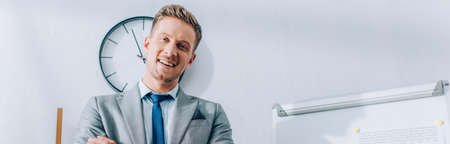 Positive businessman in formal wear looking at camera near flipchart in office, banner
