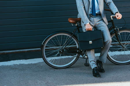 Cropped view of businessman with briefcase standing near bike outdoors
