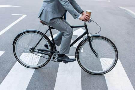 Cropped view of businessman holding takeaway coffee while cycling on crosswalkの写真素材