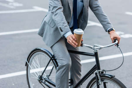 Cropped view of businessman holding takeaway coffee while riding bicycle outdoorsの写真素材