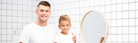 Smiling father hugging son near round mirror in bathroom, banner