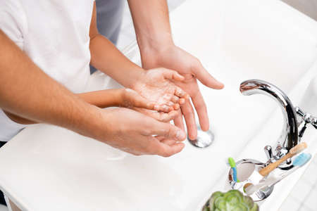 Cropped view of father and son washing hands together, while standing near washbasin in bathroomの写真素材