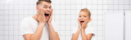 Shocked father and son shouting while touching cheeks with hands in bathroom, banner