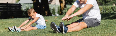 Preschooler boy with outstretched hands warming up while sitting near young adult man in park on...