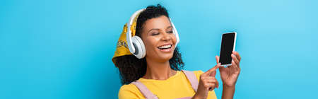 happy african american woman in headphones listening music and pointing with finger at smartphone...