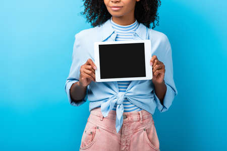 cropped view of curly african american woman holding digital tablet with blank screen on blue