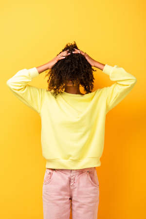 african american woman covering face while adjusting curly hair on yellow
