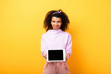 happy african american woman holding digital tablet with blank screen on yellow