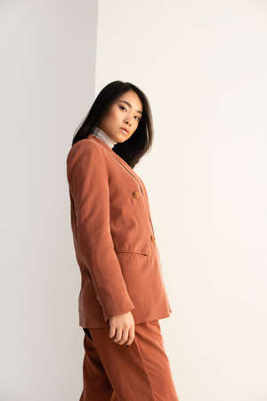 brunette asian woman in trendy suit looking at camera on whiteの写真素材
