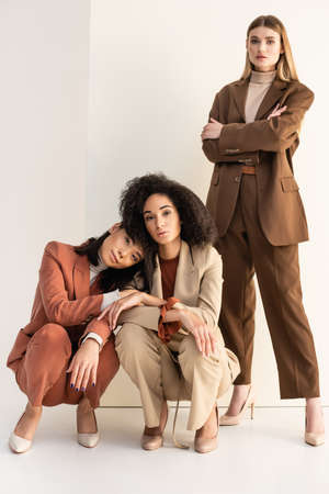 full length of interracial young women in trendy suits posing on whiteの写真素材